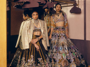 Two women in elaborate traditional outfits standing in a room with mirrors.