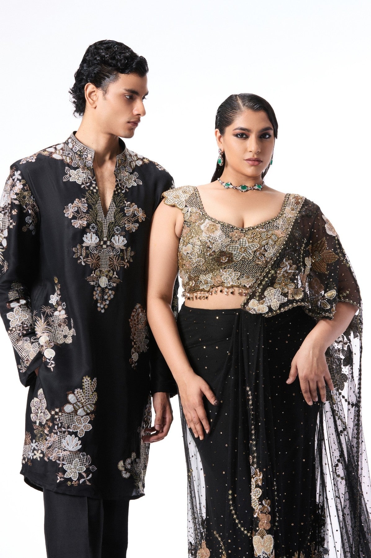 Two people wearing black and gold embroidered traditional outfits 