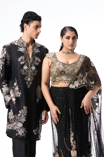 Two people wearing black and gold embroidered traditional outfits 