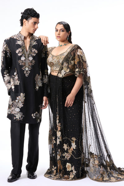 Man and woman in black and gold traditional outfits with floral patterns 