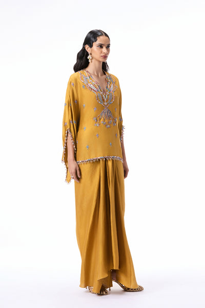 Side angle view of the mustard dupion silk short tunic kurta and pleated draped skirt with applique detailing.