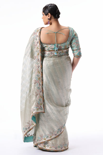 “Silver Banarasi tissue brocade saree with applique embellished border and contrasting blue tissue blouse.”
