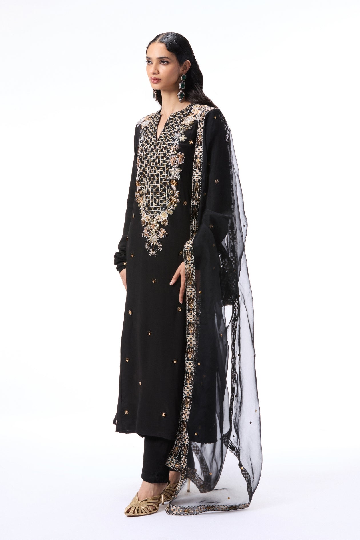 Woman wearing a black embroidered outfit with a sheer dupatta on a white background