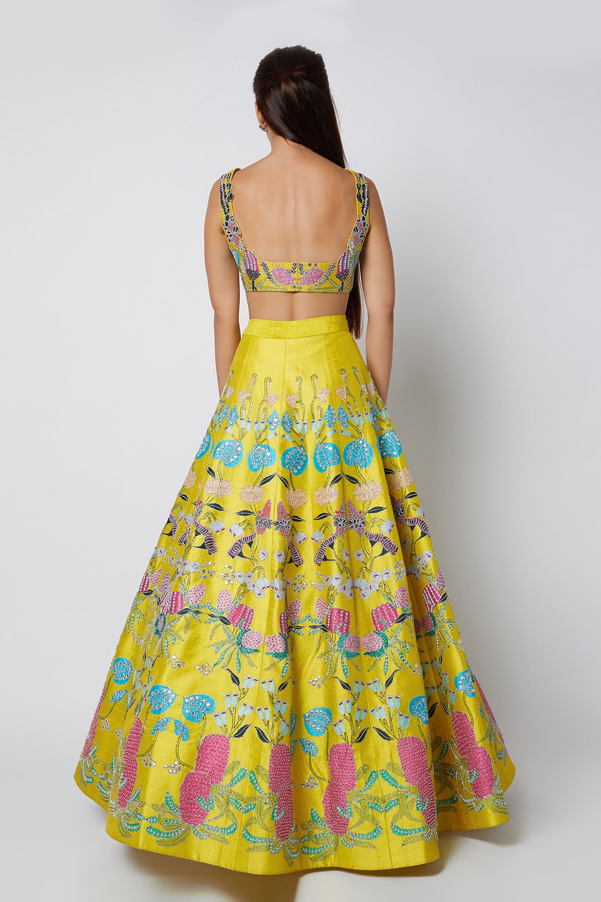 Back view of yellow pastiche raw silk appliquéd lehenga with blouse and cutwork tulle dupatta